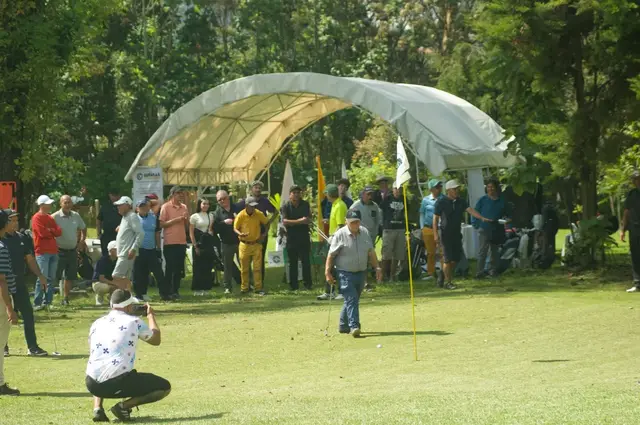 Un jugador en el green durante un torneo, con el público frente a la carpa del club