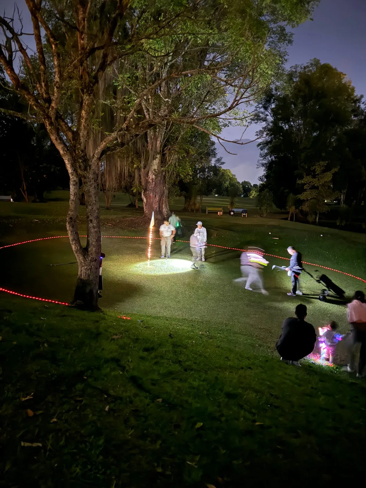 Jugadores de noche alrededor de un green iluminado y rodeado por un círculo de luces